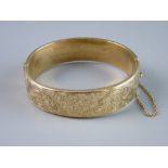 A NINE CARAT GOLD HOLLOW BANGLE, half bright cut with floral decoration and with presentation