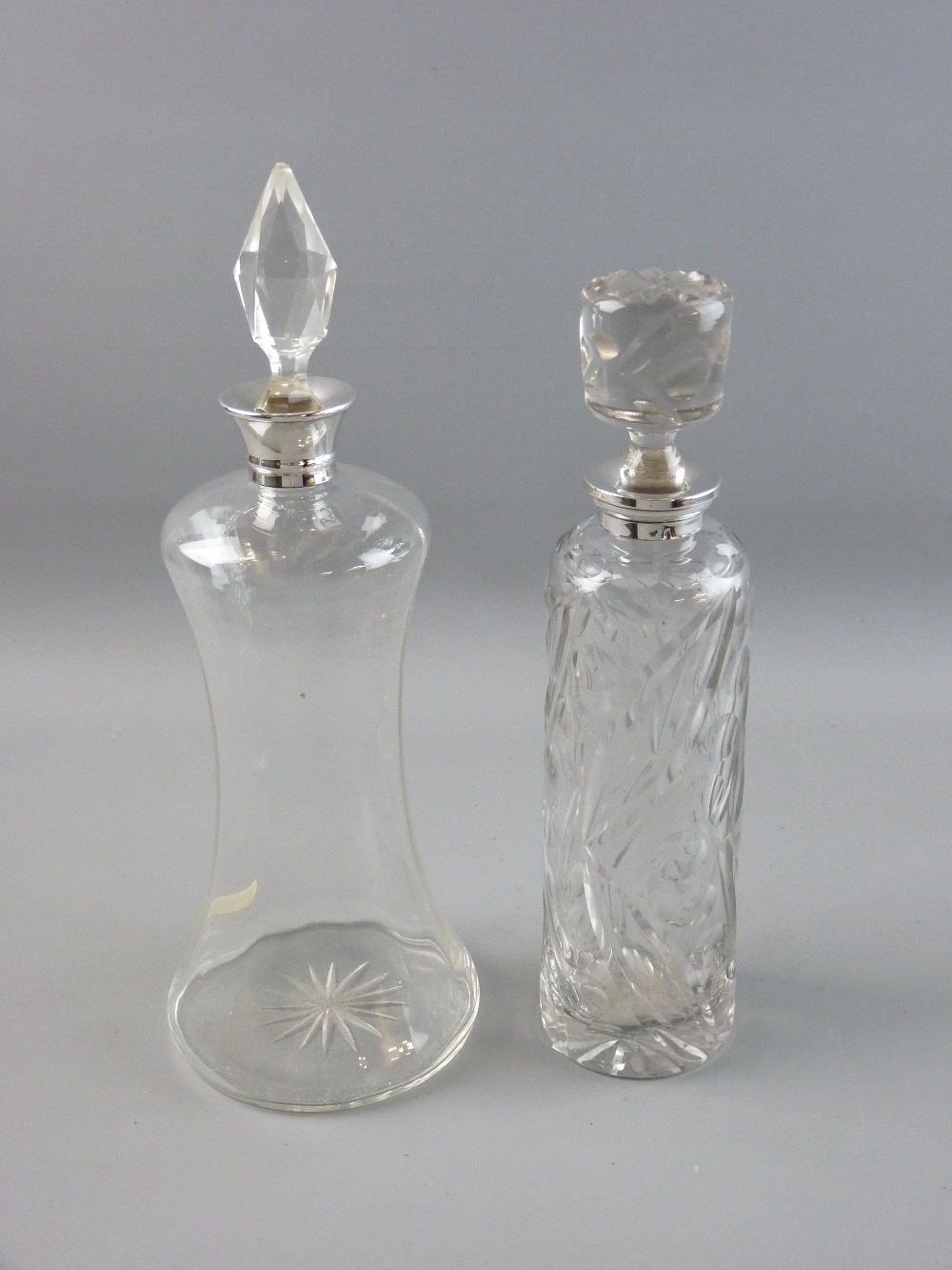 TWO SILVER COLLARED GLASS DECANTERS WITH STOPPERS, one of waisted form hallmarked Birmingham 1933