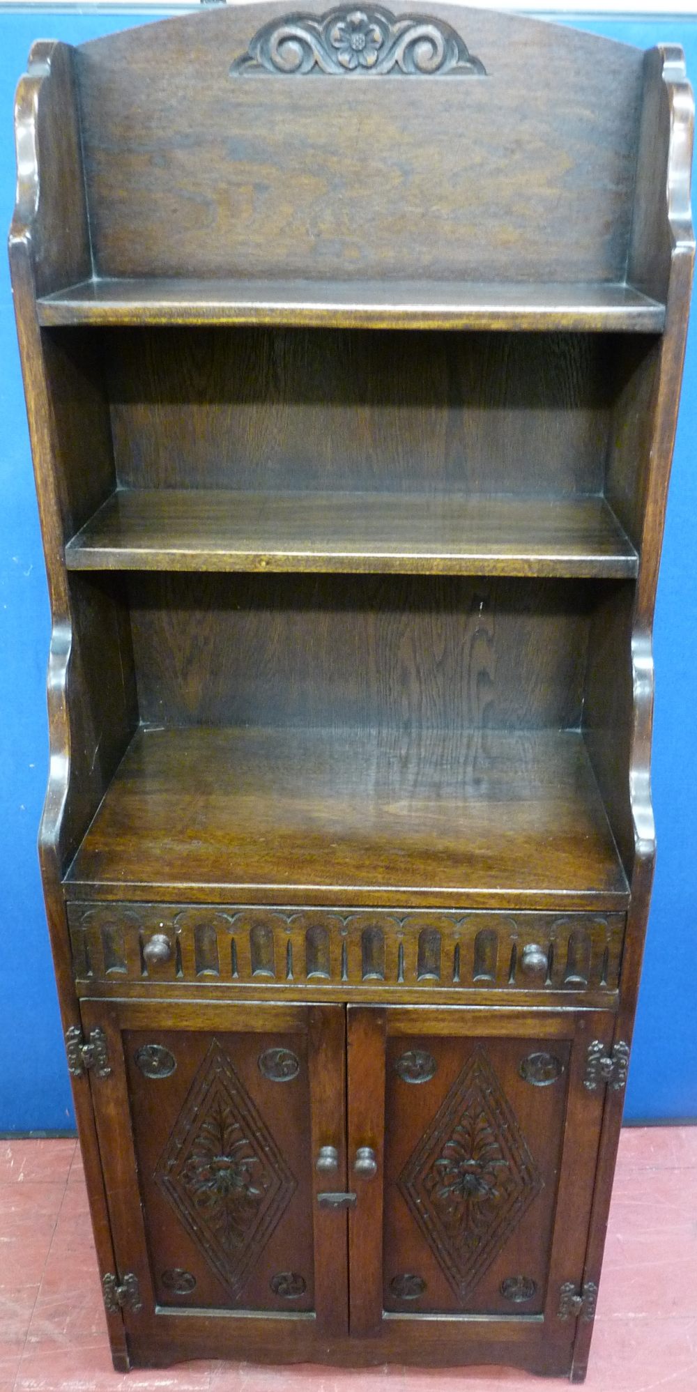 A REPRODUCTION OAK BOOKCASE CUPBOARD, the waterfall top with central carving and fixed shelves above