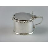 A SILVER DRUM SHAPED MUSTARD POT, lidded with shell thumbpiece, gadrooned edge and gilt interior (no