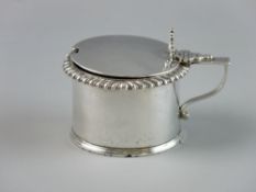 A SILVER DRUM SHAPED MUSTARD POT, lidded with shell thumbpiece, gadrooned edge and gilt interior (no