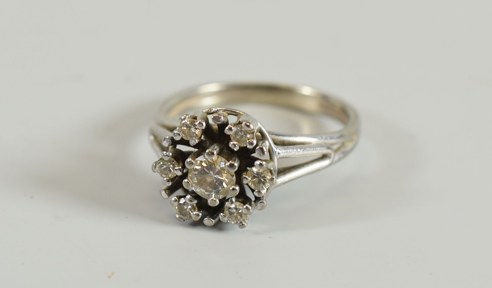 A DIAMOND CLUSTER RING composed of centre diamond and six surrounding stones, in unmarked white
