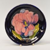 A MOORCROFT DISH typically tube-line decorated with coral coloured flowers to a deep blue ground,