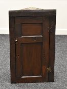 AN EARLY NINETEENTH CENTURY HANGING CORNER CUPBOARD of primitive form with single hinged door