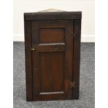 AN EARLY NINETEENTH CENTURY HANGING CORNER CUPBOARD of primitive form with single hinged door