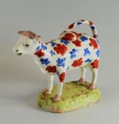 A SWANSEA POTTERY COW CREAMER standing on a grassy base, with looped tail as handle and decorated