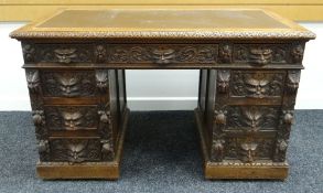 A HEAVILY CARVED KNEEHOLE WRITING DESK carved with lion mask handles and with flanking banks of four