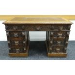 A HEAVILY CARVED KNEEHOLE WRITING DESK carved with lion mask handles and with flanking banks of four
