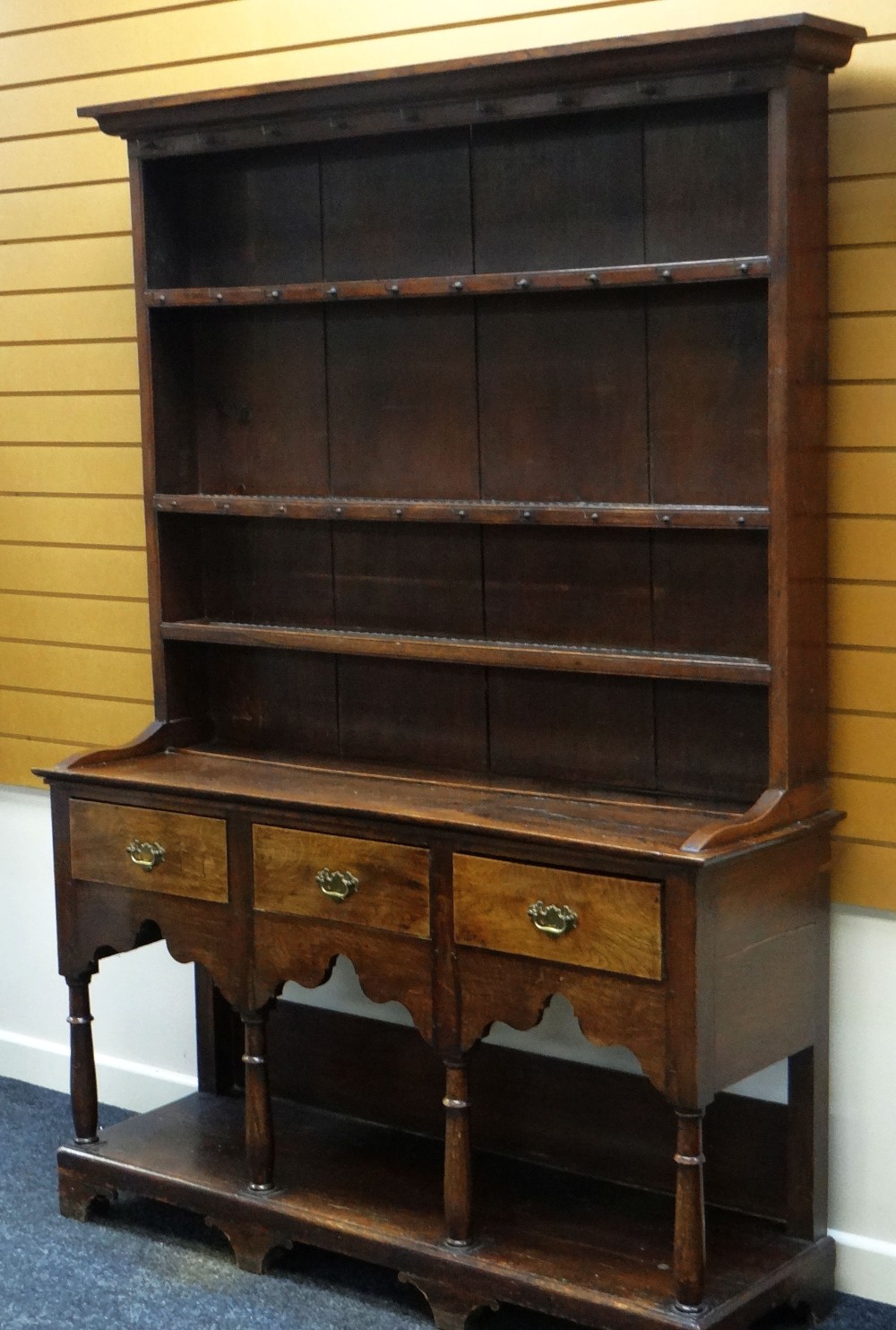 AN OAK WELSH DRESSER having a three shelved closed rack over a three drawer base raised on four