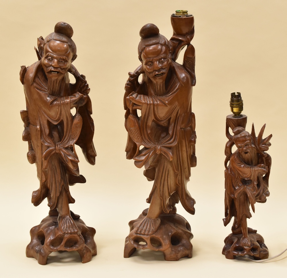 A PAIR OF CHINESE HARDWOOD CARVED TABLE LAMPS in the form of robed fisherman with their carp on