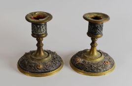 A PAIR OF METAL OVERLAID BRASS CANDLEHOLDERS on circular bases with raised urn sconces, 11cms high