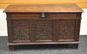 A LATE EIGHTEENTH CENTURY OAK BLANKET CHEST having a heavily carved panel facade, panelled sides and