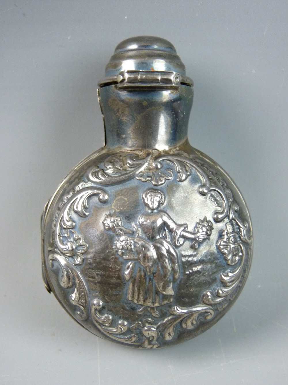 A SILVER SMELLING SALTS BOTTLE HOLDER, the circular case with embossed swag cartouche and central
