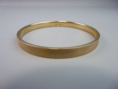 A NINE CARAT GOLD BANGLE with engine turned decoration, 13.5 grms