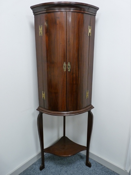 A RE-FURBISHED BOW FRONT MAHOGANY TWO DOOR HANGING CORNER CUPBOARD with brass 'H' hinges on an appro