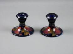 A PAIR OF MOORCROFT POMEGRANATE SHORT CANDLESTICKS on a cobalt ground, impressed and painted factory