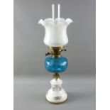 A VICTORIAN OIL LAMP with blue glass font supported on a brass mounted circular white pottery