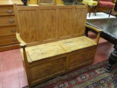 AN ANTIQUE STRIPPED PINE DOUBLE BOX SEAT BENCH with four panel back and shaped arms, the twin lidded