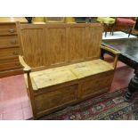 AN ANTIQUE STRIPPED PINE DOUBLE BOX SEAT BENCH with four panel back and shaped arms, the twin lidded