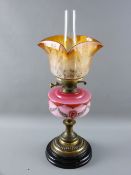 A VICTORIAN OIL LAMP with decorative pink milk glass font on a lacquered brass column and circular