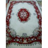 A CREAM GROUND TUFTED WOOLLEN CARPET with a red ground floral framed border and central cartouche,