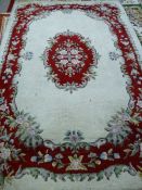A CREAM GROUND TUFTED WOOLLEN CARPET with a red ground floral framed border and central cartouche,