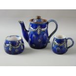 A ROYAL DOULTON STONEWARE THREE PIECE TEA SERVICE with raised swag and floral decoration on a cobalt