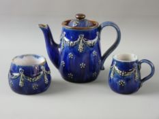 A ROYAL DOULTON STONEWARE THREE PIECE TEA SERVICE with raised swag and floral decoration on a cobalt