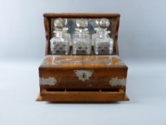 AN OAK & ELECTROPLATED TANTALUS having three well cut hobnail patterned square decanters (neck to