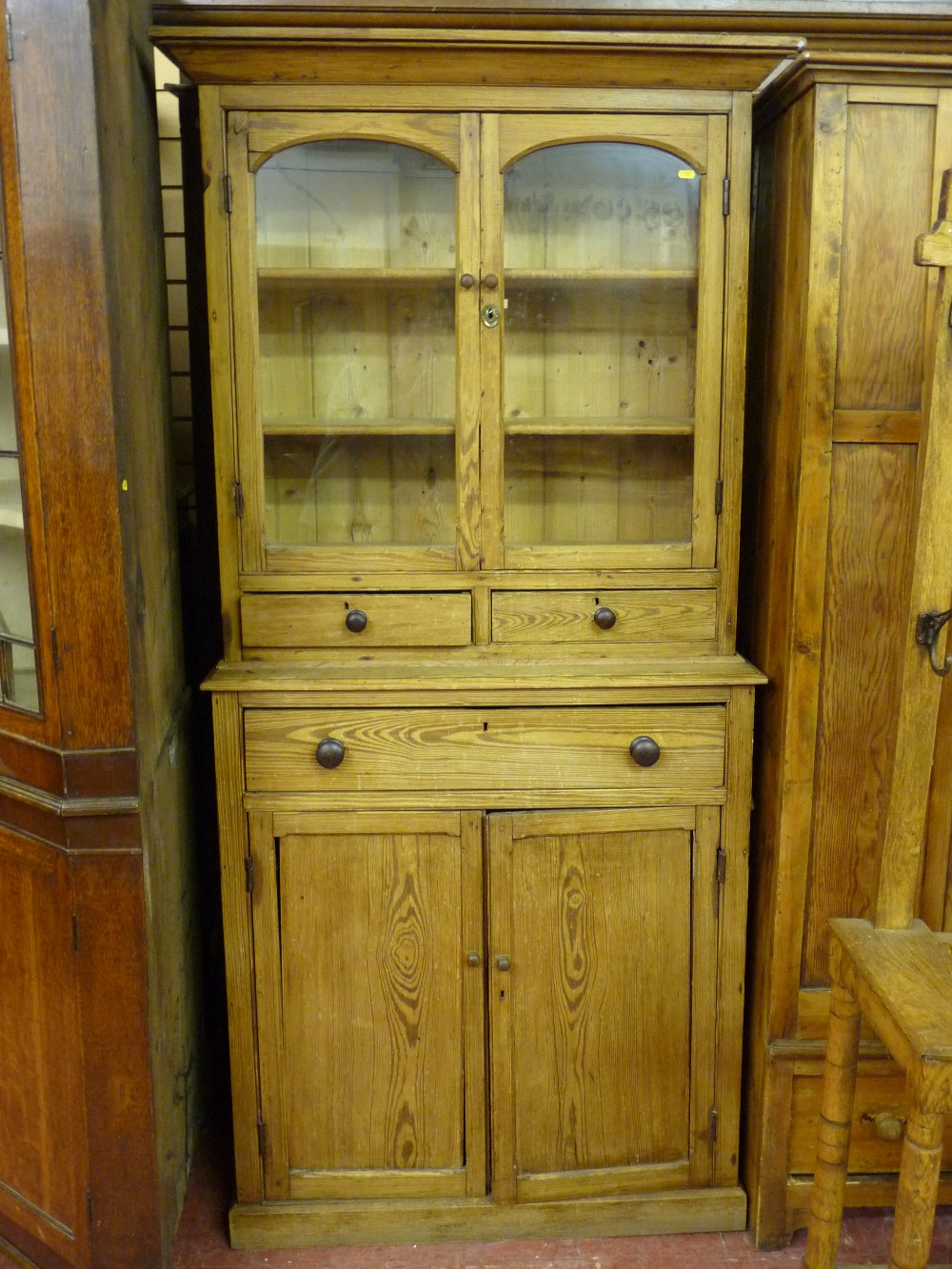 AN ANTIQUE STRIPPED PINE WELSH COUNTRY CUPBOARD, the inverted cornice over twin glazed arched top