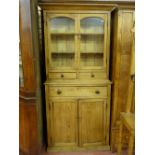 AN ANTIQUE STRIPPED PINE WELSH COUNTRY CUPBOARD, the inverted cornice over twin glazed arched top