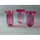 A SET OF THREE CRANBERRY GLASS FLUTED VASES on plain bases