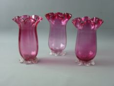 A SET OF THREE CRANBERRY GLASS FLUTED VASES on plain bases