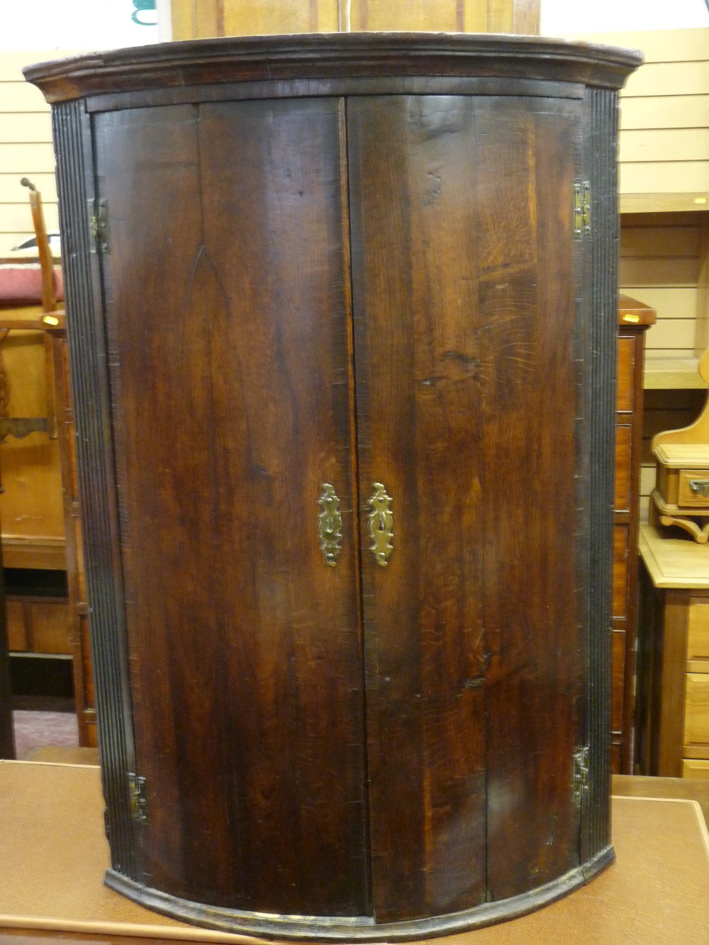 A GEORGIAN OAK BOW FRONT HANGING CORNER CUPBOARD, the doors with brass 'H' hinges and decorative