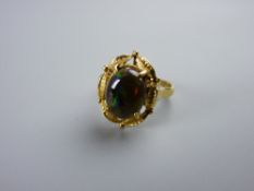 AN EIGHTEEN CARAT GOLD BLACK OPAL DRESS RING having an oval cabochon cut opal in a fancy leaf