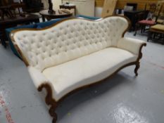 A buttoned French-style antique sofa with curved back and in cream upholstery