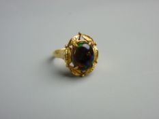 AN EIGHTEEN CARAT GOLD BLACK OPAL DRESS RING having an oval cabochon cut opal in a fancy leaf