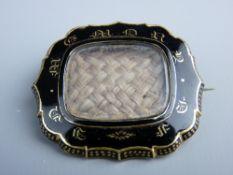 A VICTORIAN MOURNING BROOCH with central plaited hair panel in a black enamel and gilt metal