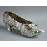 A CONTINENTAL SILVER MODEL OF A PERIOD STYLE SHOE with applied front bow and repousse style repeated