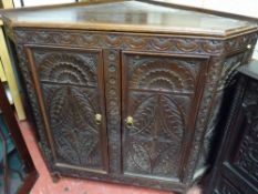 A TWO DOOR CARVED OAK FLOORSTANDING CORNER CUPBOARD, the door panels and sides with leaf and roundel