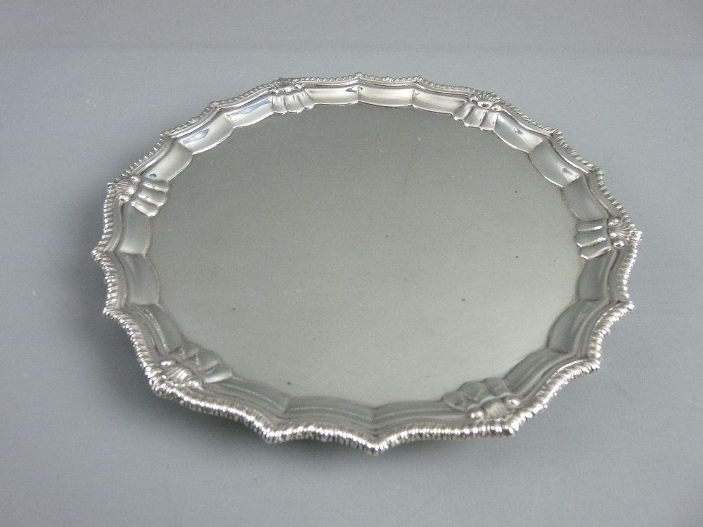 A SILVER CARD TRAY ON THREE HOOF FEET, 19 cms diameter with rope and shell decorated border,