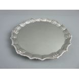 A SILVER CARD TRAY ON THREE HOOF FEET, 19 cms diameter with rope and shell decorated border,