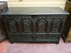 AN ANTIQUE CARVED OAK COFFER, the three plank stained lidded top over a front section of four carved