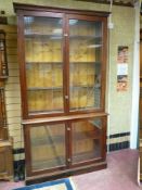 A VINTAGE TWO PIECE STAINED PINE BOOKCASE having twin glazed doors to the upper and base sections