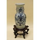 A CHINESE STYLE POTTERY TWIN-HANDLED VASE on wooden stand, decorated in blue with vase of flowers