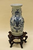 A CHINESE STYLE POTTERY TWIN-HANDLED VASE on wooden stand, decorated in blue with vase of flowers