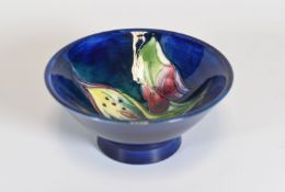 A MOORCROFT FOOTED DISH of blue ground with tube-lined flowers and leaves, 11cms diam