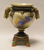 A HADLEY WORCESTER VASE WITH TWIN GOAT-HEAD HANDLES and raised on four hoof feet, painted with