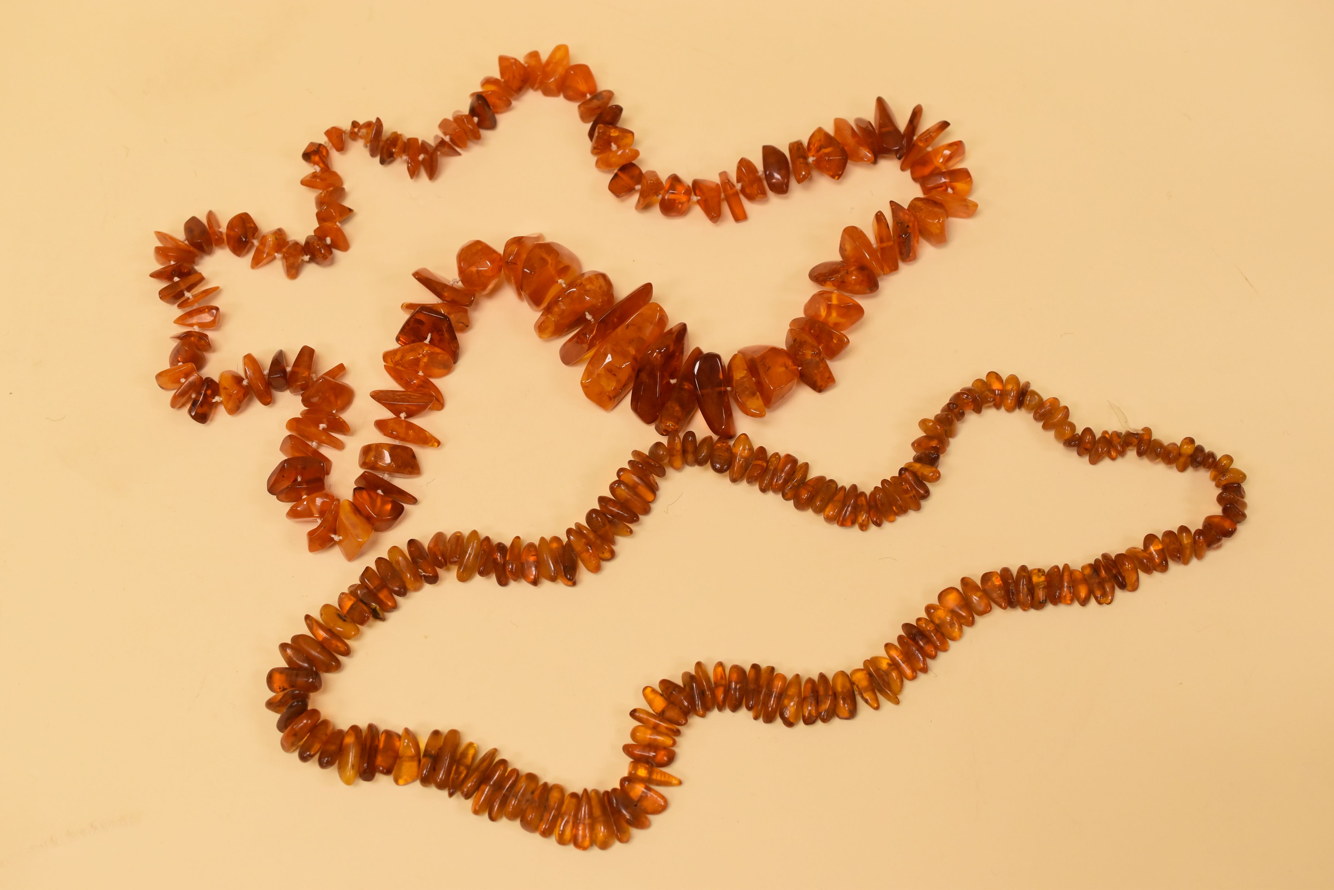 TWO STRINGS OF BALTIC AMBER BEADS, raw and unpolished, 74 and 64cms long