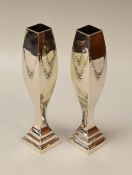 A PAIR OF SILVER BUD VASES waisted and on stepped square bases with raised floral swags,